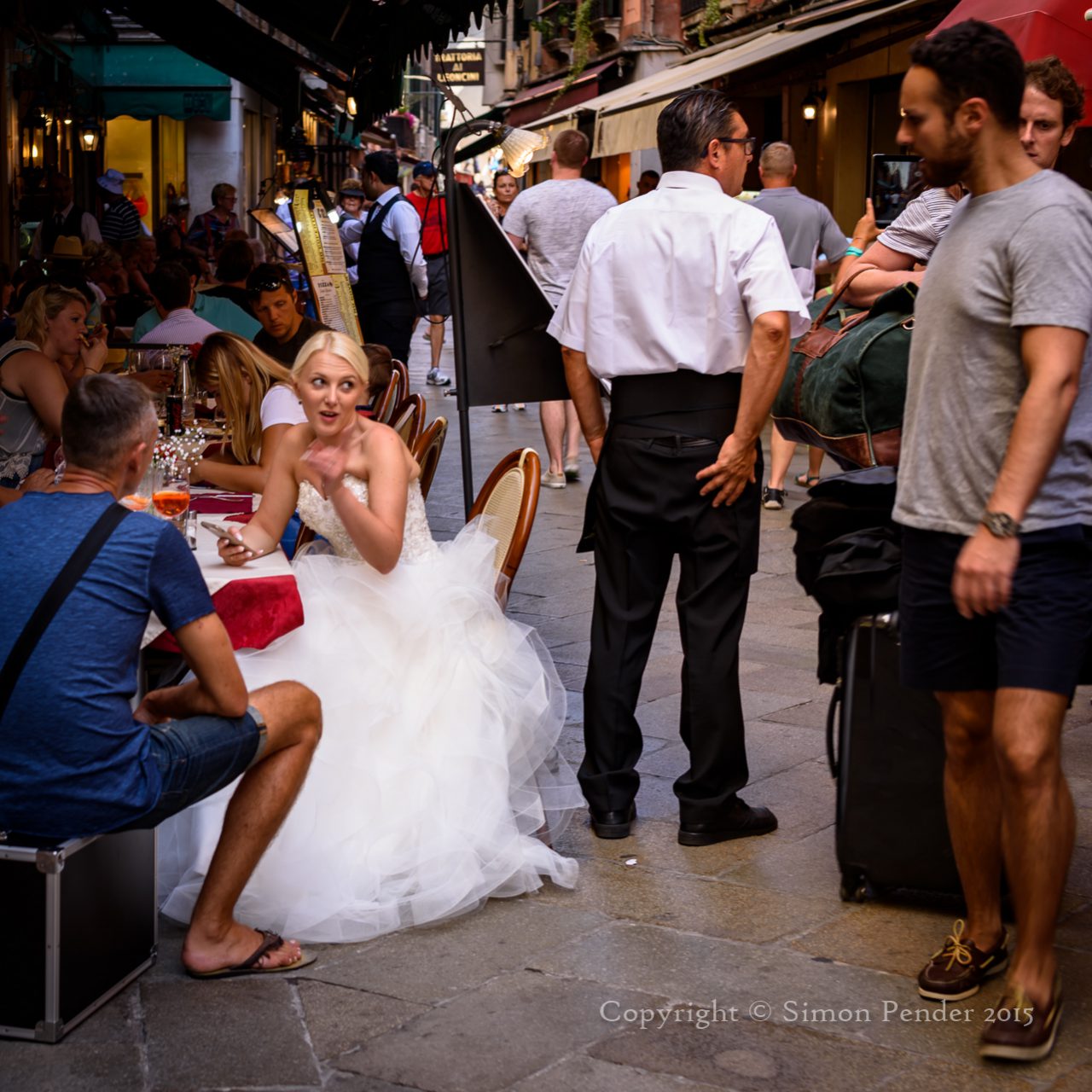 Bride in white gown sitting in pavement cafe, Venice.